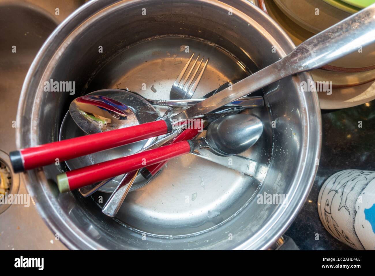Dirty cutlery in a saucepan at the side of a kitchen sink. Stock Photo