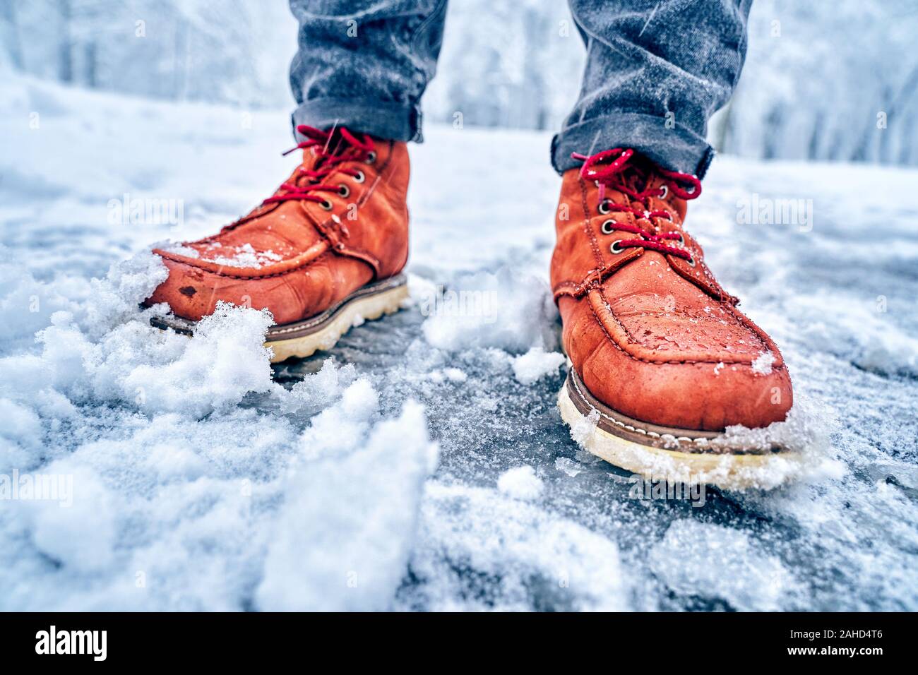 Feet of a man on a snowy sidewalk in brown boots. Winter slippery pawement. Seasonal weather concept Stock Photo