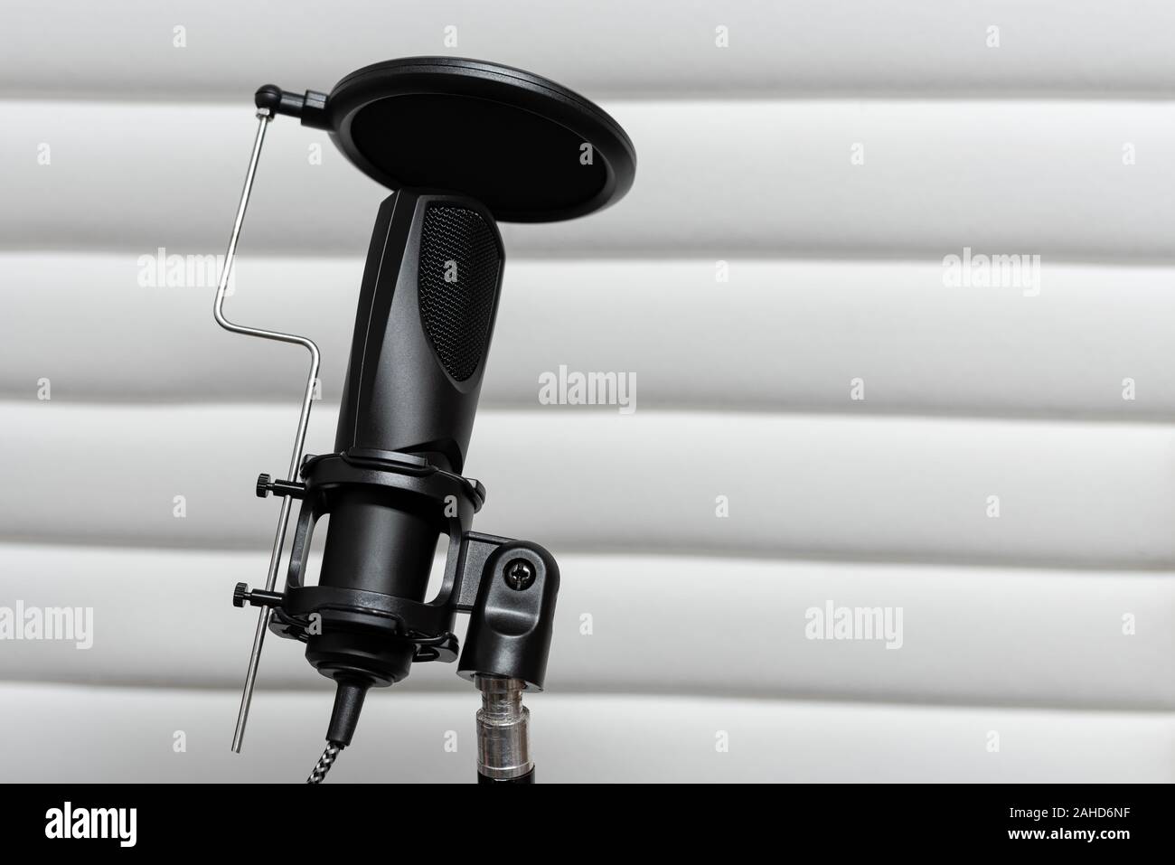 Condenser microphone placed on a tripod with white acustic panels in the  background in a music studio, ready for recording. Stock Photo