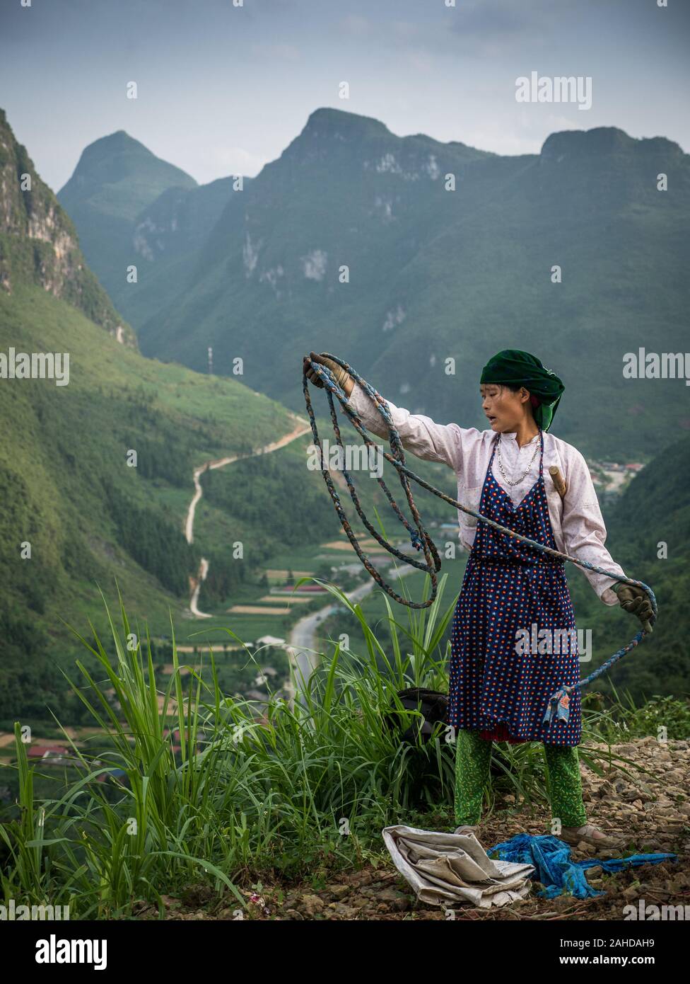 Female Vietnamese farmer of ethnic minority rolling up rope in the mountains of North Vietnam, vibrant green karst mountains in the background Stock Photo