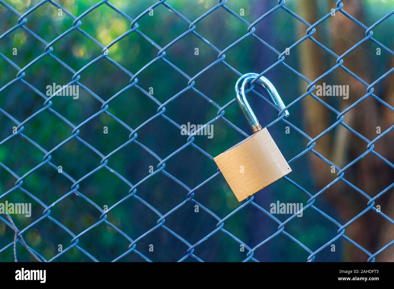 Open a bit rusty padlock hanging on fence wire netting with copy space Stock Photo