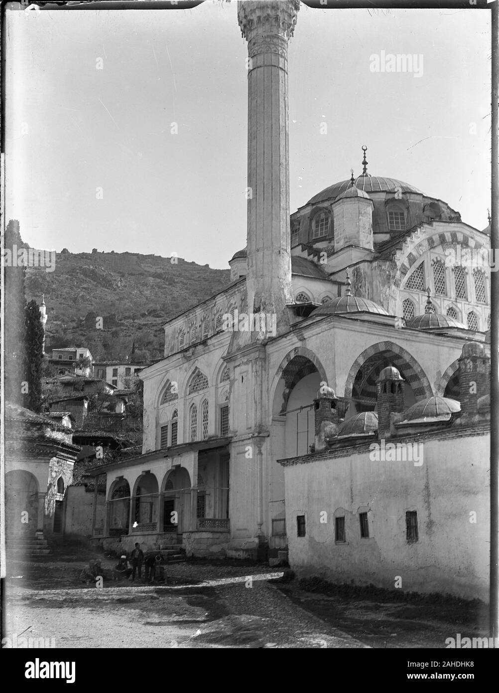 Manisa, Muradiye Külliyesi mosque, street view with a group of natives sitting in the road near the entrance. Muradiye mosque was built by Mimar Sinan in the late 16. century. Manisa is located in the western part of Turkey. Photography taken in the 1910s on dry glass plate, part of the Herry W. Schaefer Ottoman collection. Stock Photo