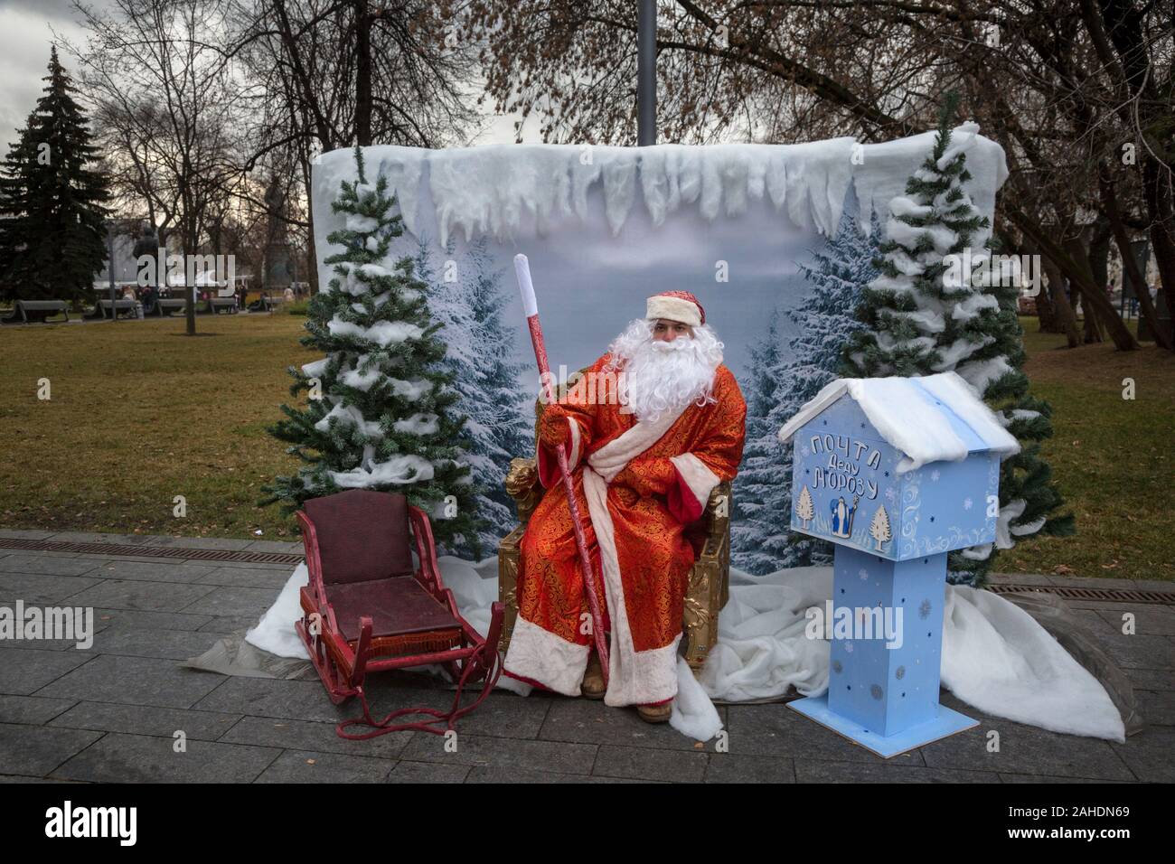 Ded Moroz (Russian Santa Claus) in winter scenery sits on a chair in one of the parks of Moscow during abnormal warm and snowless winter, Russia Stock Photo