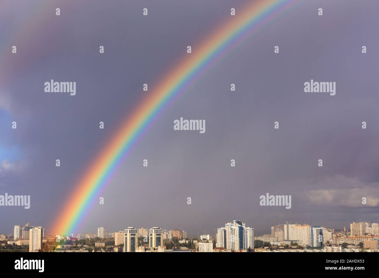 A bright large and dense rainbow in a gray cloudy sky above city houses ...