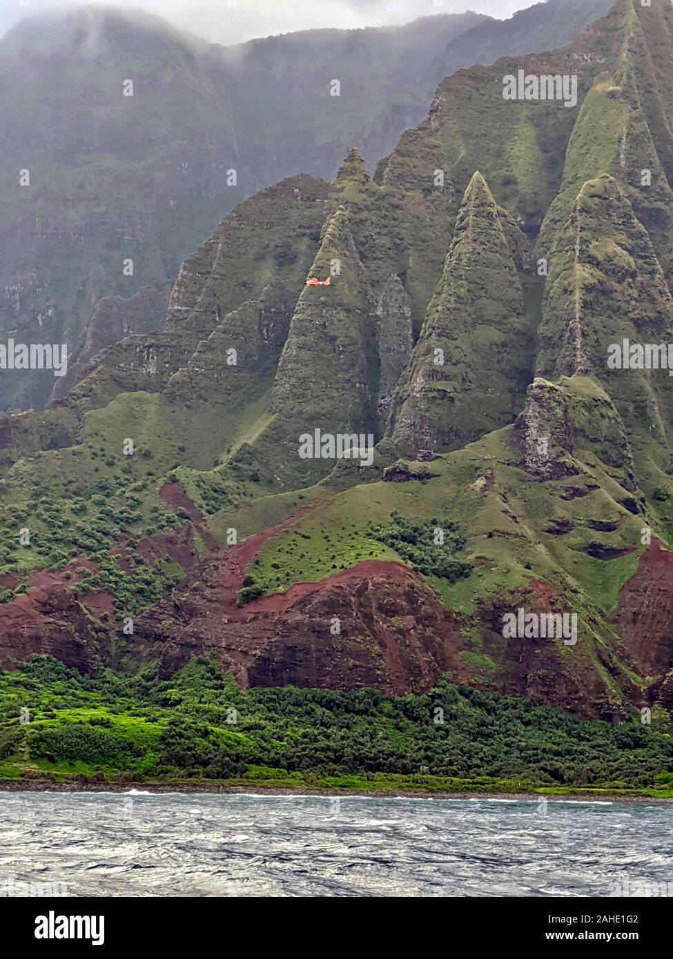 Kauai, United States of America. 27 December, 2019. An U.S. Coast Guard MH-65 Dolphin helicopter with Air Station Barbers Point searches the Na Pali coast of Kauai for a missing tour helicopter with seven people aboard December 27, 2019 in Hawaii. The flight seeing helicopter with Safari Helicopters failed to return after a short flight to view the rugged coastline.  Credit: Lt. Dan Winter/USCG/Alamy Live News Stock Photo