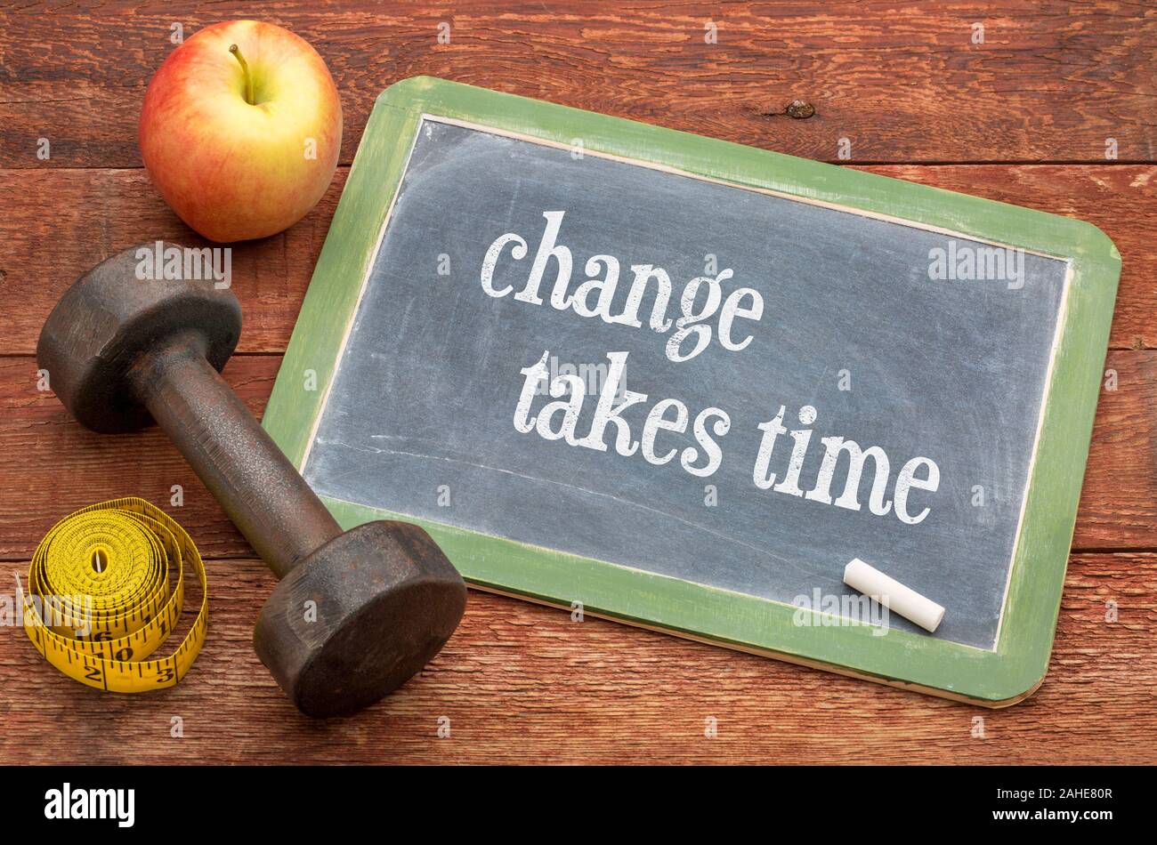 change takes time -  slate blackboard sign against weathered red painted barn wood with a dumbbell, apple and tape measure, fitness, persistence and d Stock Photo