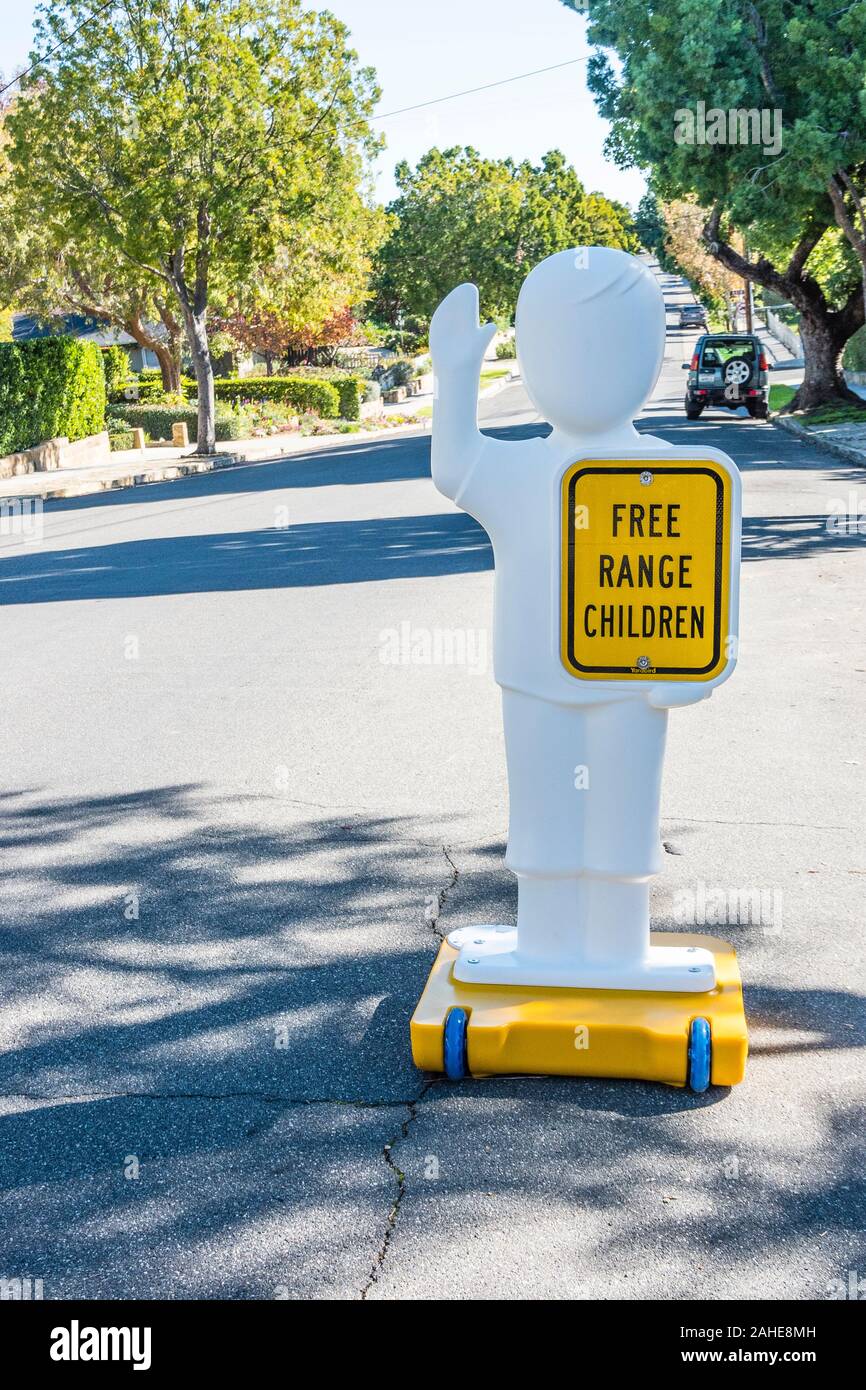 A very humorous sign in the street in front of a house with chiildren that states "free range children" on a human-like figure to alert drivers. Stock Photo