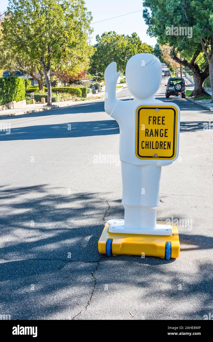A very humorous sign in the street in front of a house with chiildren that states 'free range children' on a human-like figure to alert drivers. Stock Photo