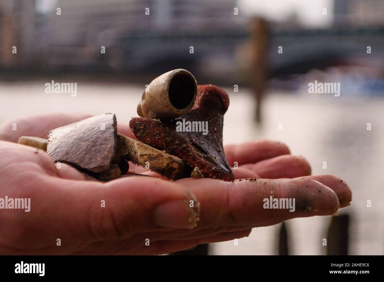 Mudlark findings A sandy hand holds an old broken clay pipe and other