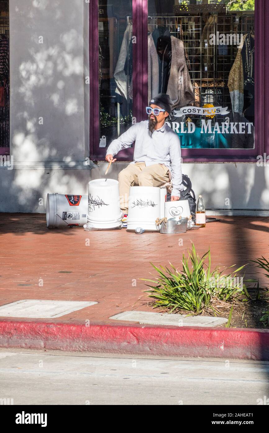 A street drummer, wearing a Fu Manchu, using white plastic 5 gallon buckets for his drum set. Stock Photo