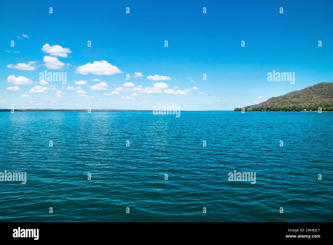 Lake Itza with cocodrile shaped mountain on sunny day and small clouds, El Remate, Peten, Guatemala Stock Photo