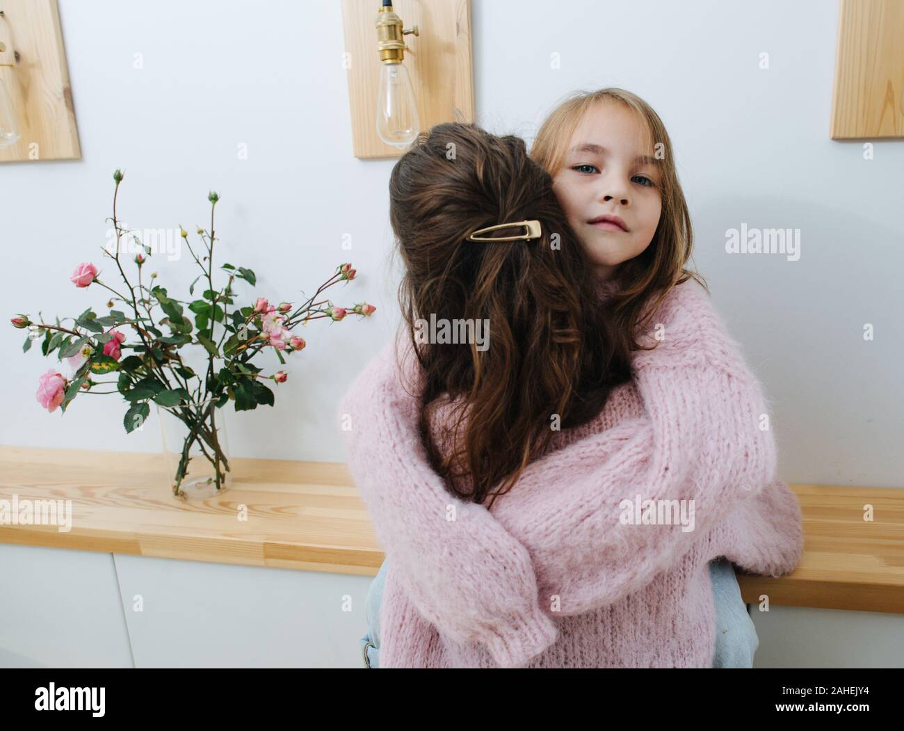 Two little girls in pink knitted sweaters hugging in a corridor Stock Photo