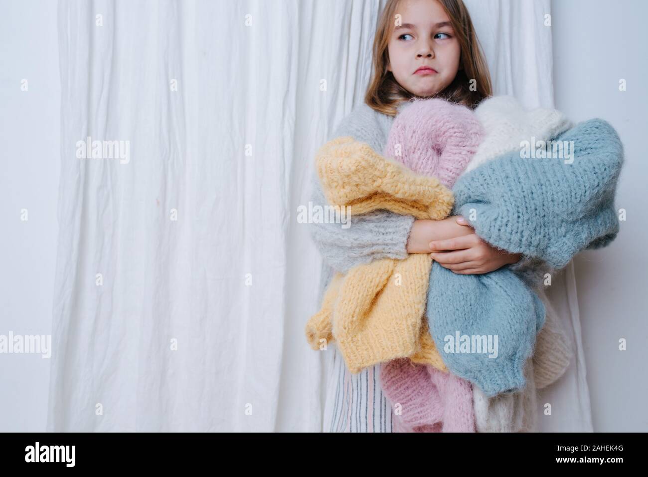 Upset little girl with a pile of soft freshly washed sweaters doing chores Stock Photo