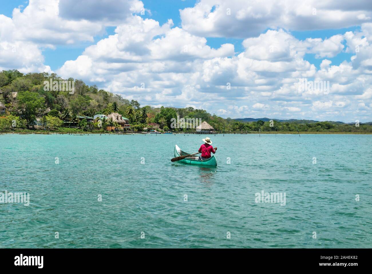 El Remate, Peten, Guatemala - 29 May 2019: Fisherman in canoe boat in turquoise colored lake Itza rowing towards village with sunny cloud sky Stock Photo