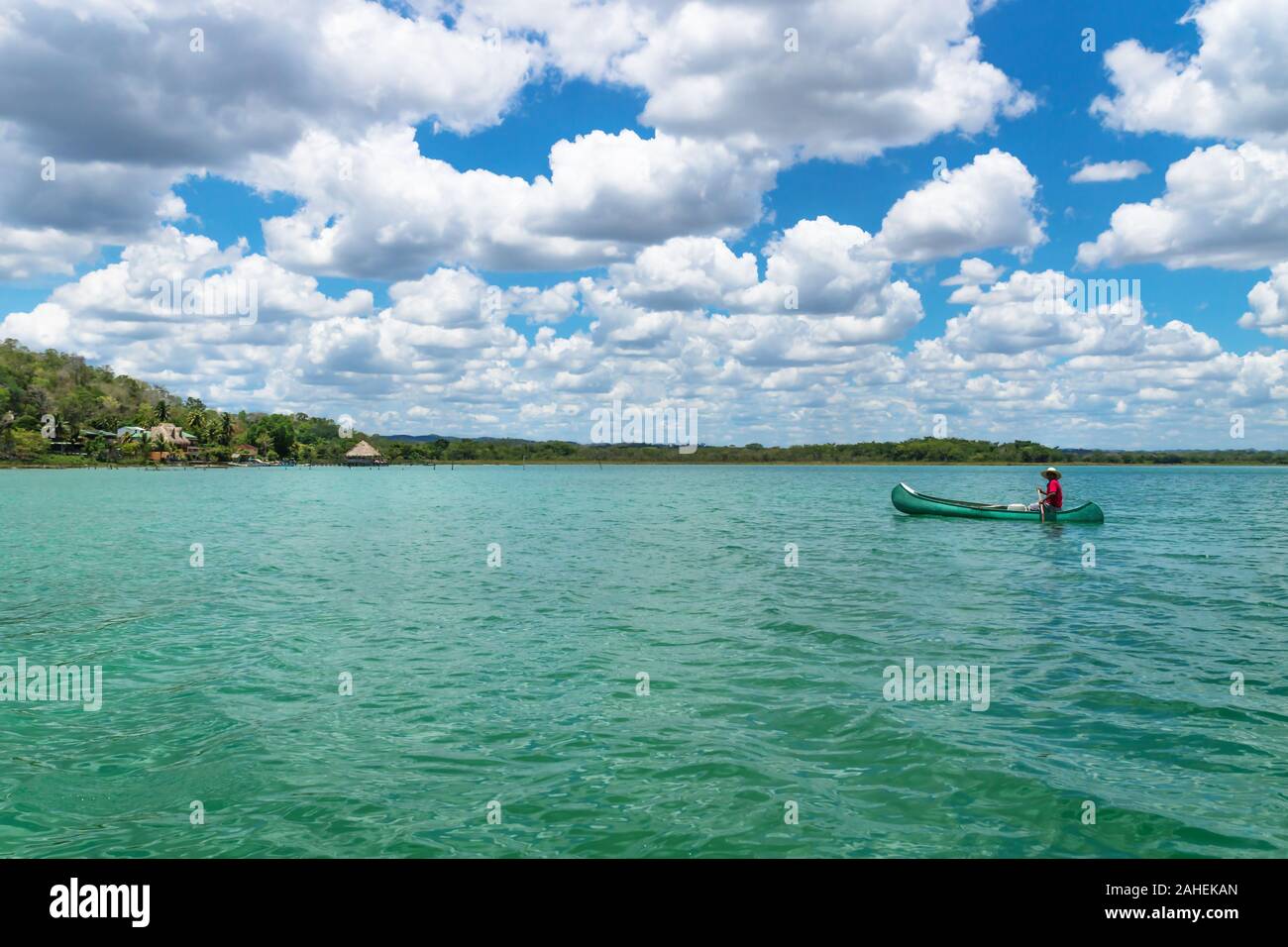 El Remate, Peten, Guatemala - 29 May 2019: Fisherman in canoe boat in turquoise colored lake Itza along village with sunny cloud sky Stock Photo