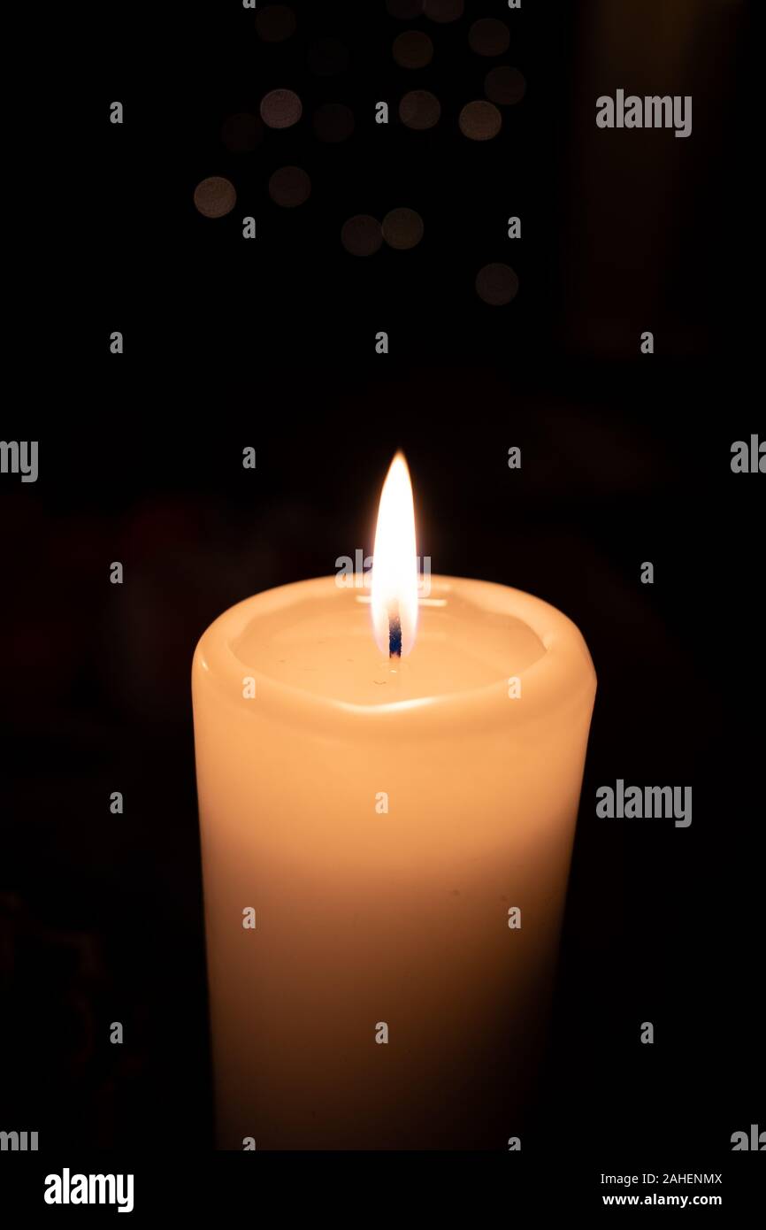 a white burning candle stands before a dark background Stock Photo - Alamy