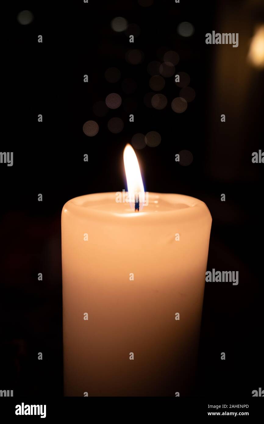 a white burning candle stands before a dark background Stock Photo - Alamy