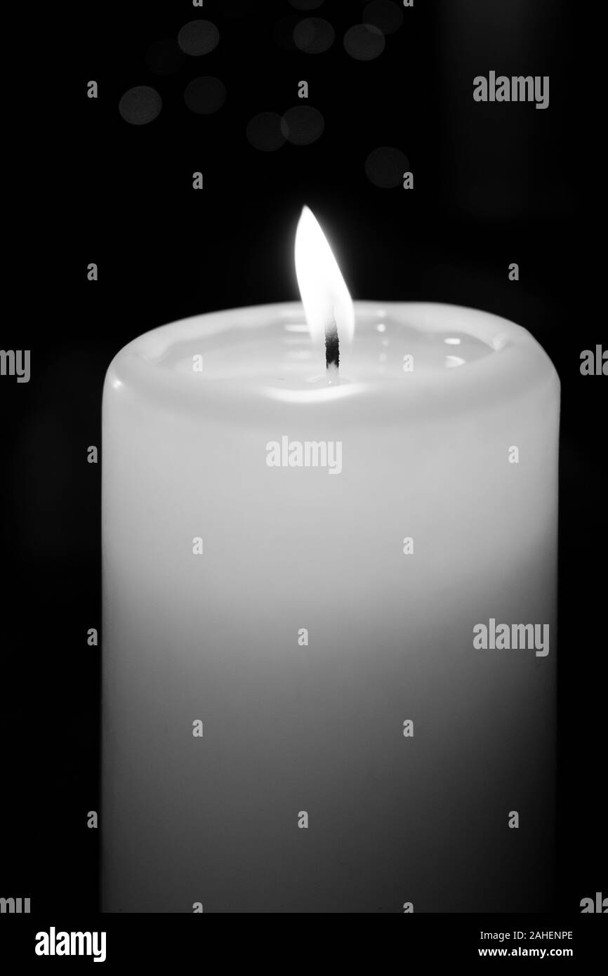 a white burning candle stands before a dark background Stock Photo Alamy