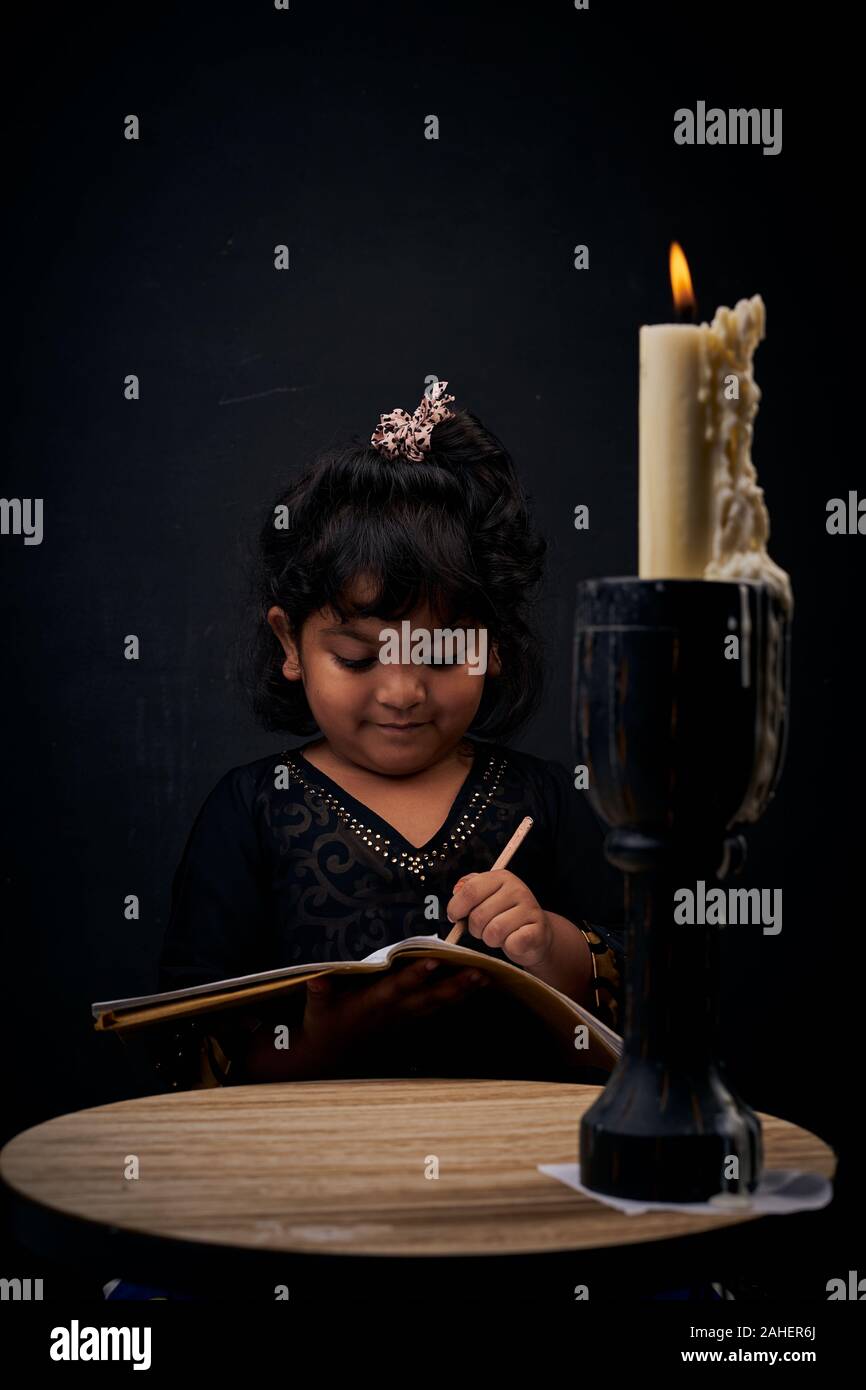 Cute little girl studying under illuminated candle light Stock Photo
