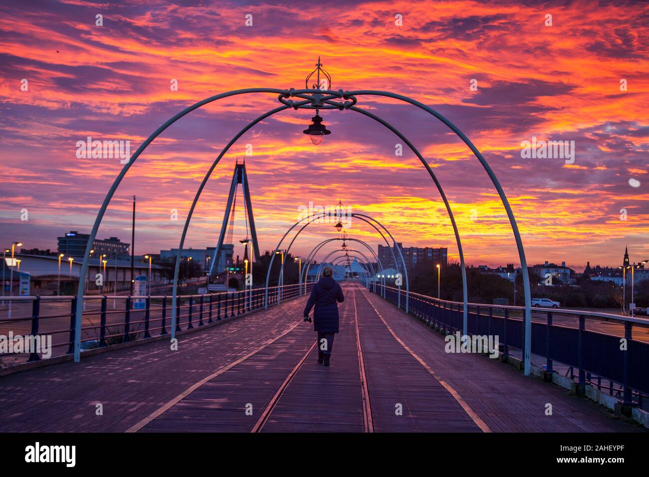 Southport, Merseyside, UK. 29th December, 2019.  Rayleigh scattering;  The sky turned blood red this morning as the sun rose over Merseyside. People walking on the pier enjoy Intense fiery winter red and orange skies at dawn as sun rises in Southport, Red sky in the morning, shepherd's warning' first appears in the Bible in the book of Matthew. It is an old weather saying often used at sunrise to signify the changing sky and was originally known to help  prepare for the next day's weather.  Credit: MediaWorldImages/AlamyLiveNews. Stock Photo