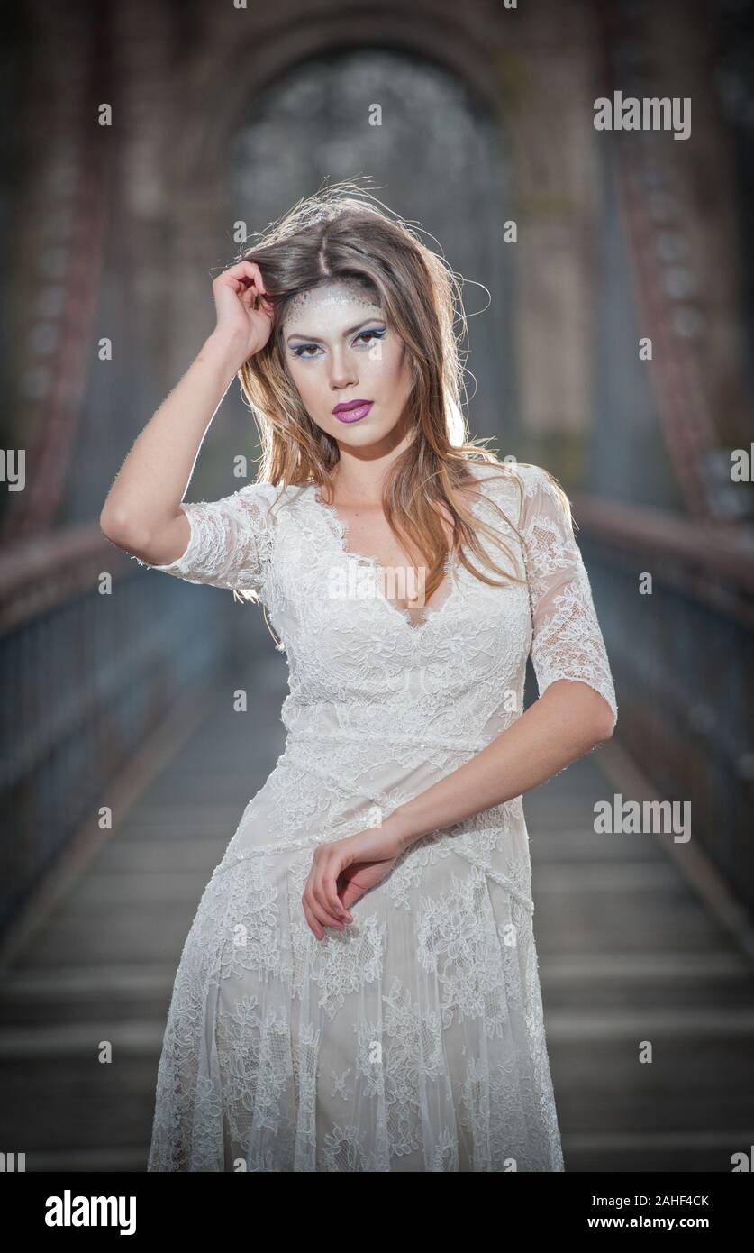 Lovely young lady wearing elegant white dress enjoying the beams of celestial light and snowflakes falling on her face. Pretty brunette girl Stock Photo