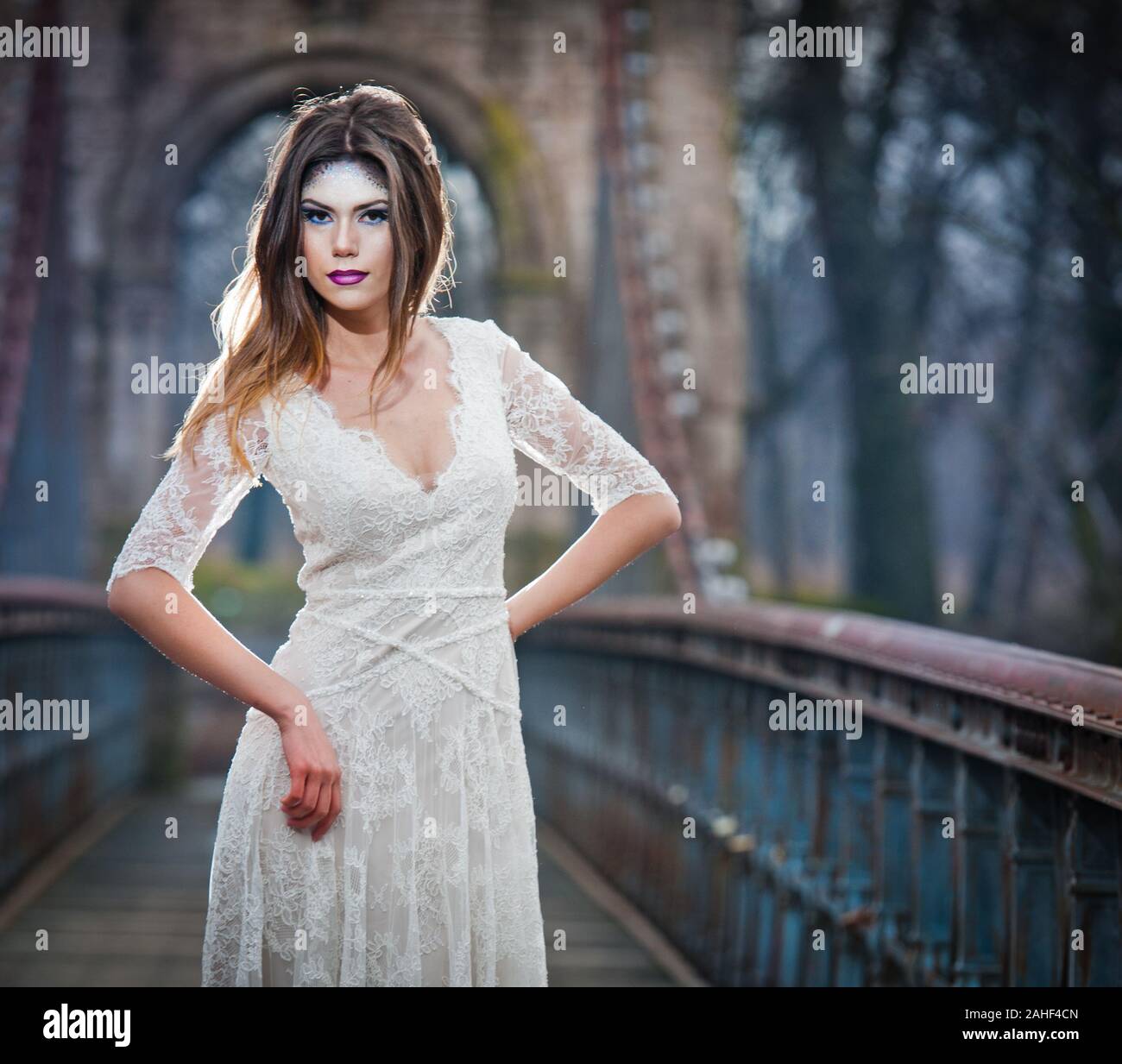 Lovely young lady wearing elegant white dress enjoying the beams of celestial light and snowflakes falling on her face. Pretty brunette girl Stock Photo