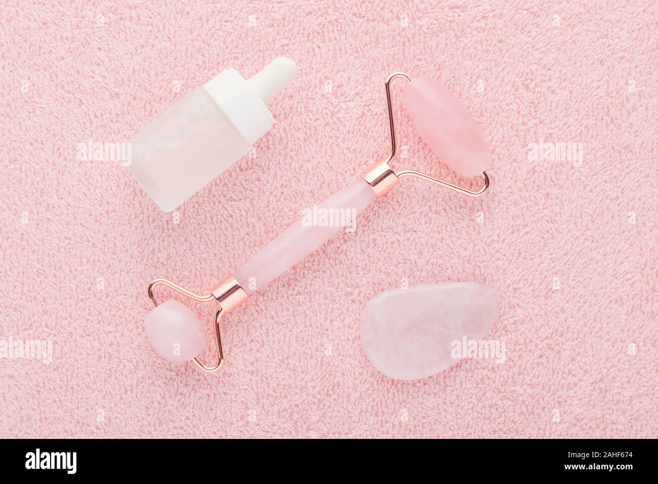 real rose quartz facial roller, gua sha massage stone and face serum, flat lay Stock Photo