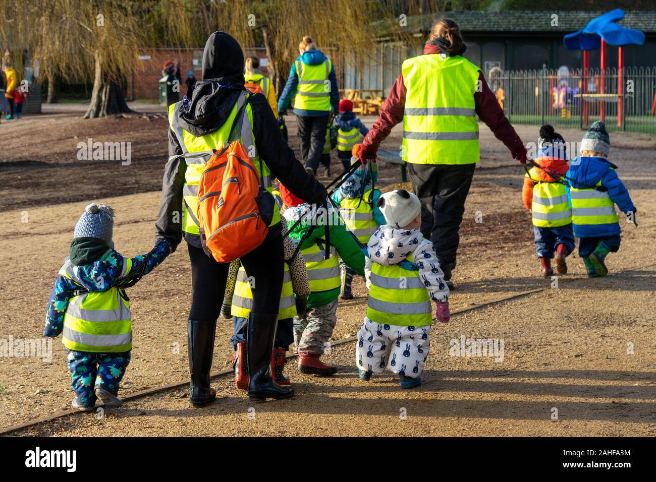 A group of young school children or nursery aged children wearing high visibility jackets while walking with teachers Stock Photo