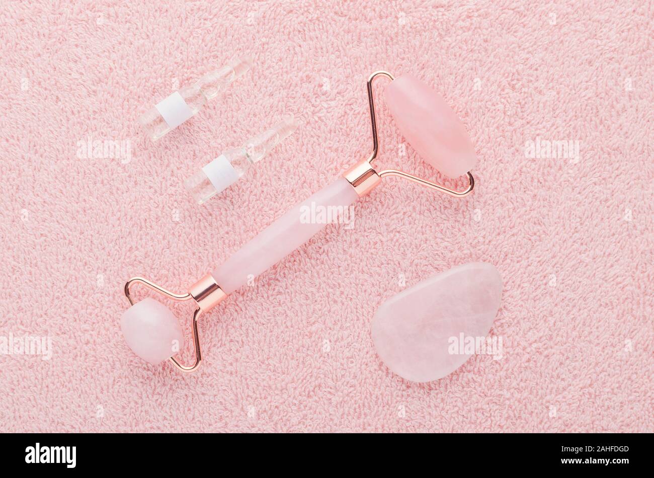 real rose quartz facial roller, gua sha massage stone and face serum in ampoules Stock Photo