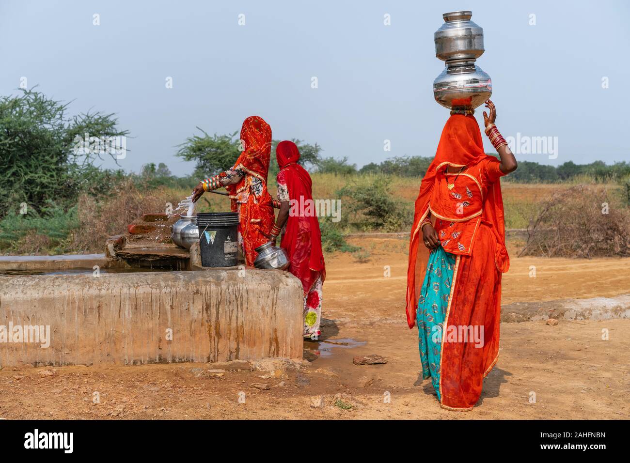 Kalbeliya gypsy women in colorful clothes collect and carry on their head drinking water at public tap in Thar desert. Pushkar, Rajasthan, India. Stock Photo