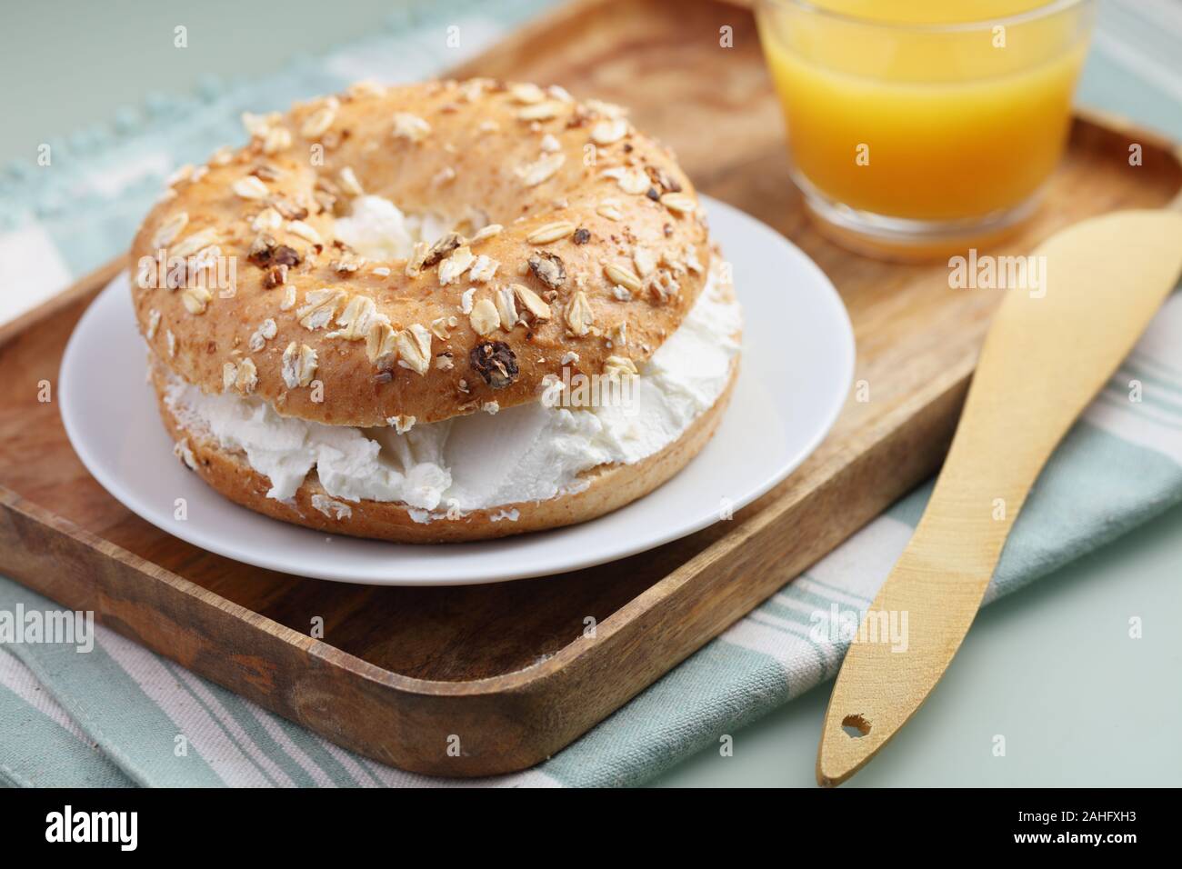 Bagel sandwich with soft cheese and a cup of orange juice on a wooden tray Stock Photo