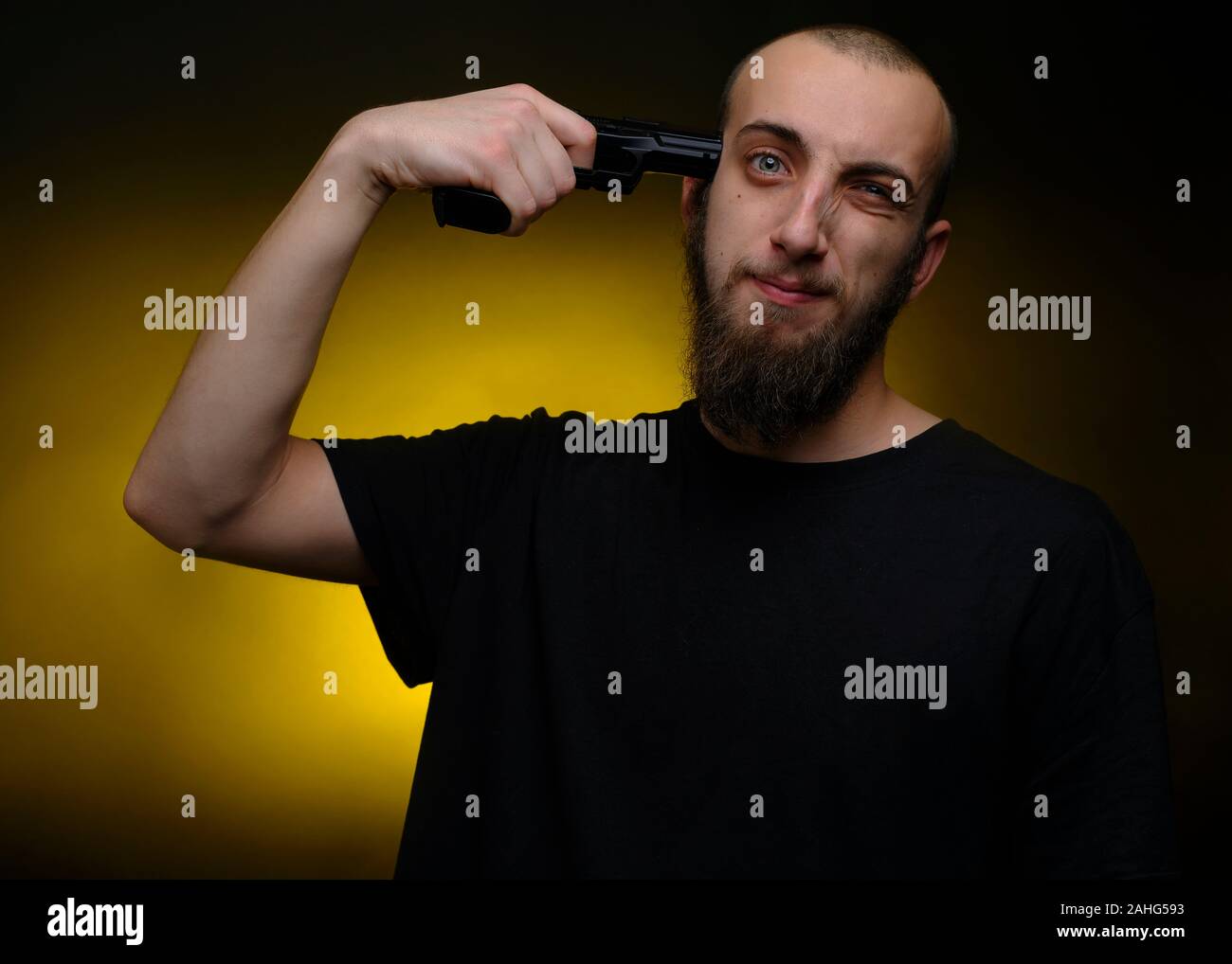 Portrait of a young man pointing a gun to his head. Shot against dark and yellow background Stock Photo