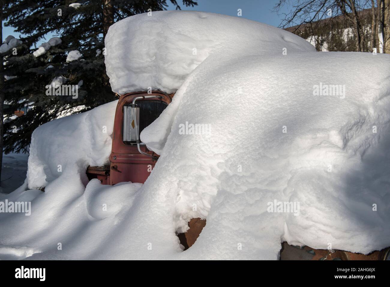 An old red truck buried in snow on a sunny day in the Alaskan forest Stock Photo