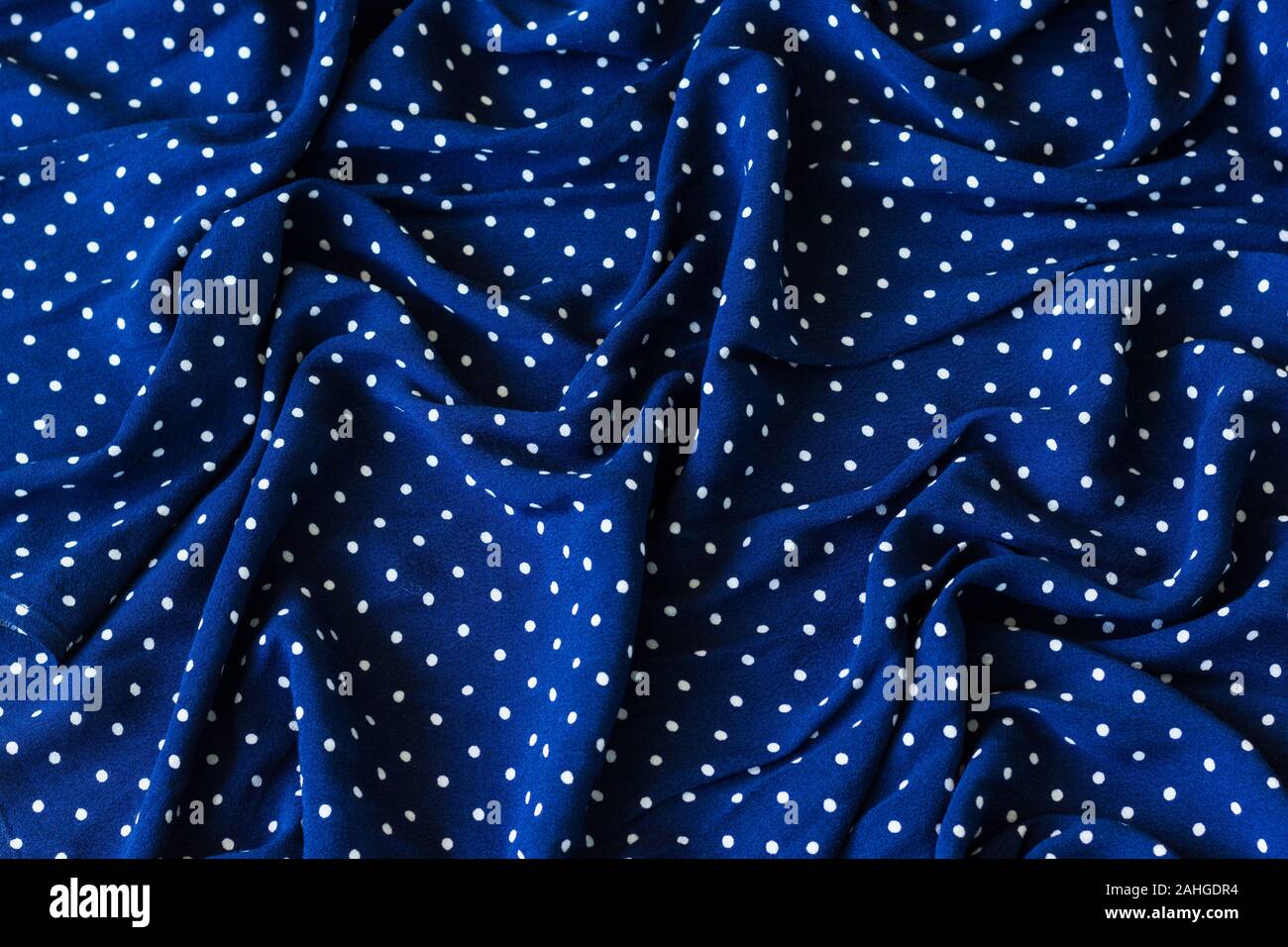 Wrinkled marine blue fabric with white dots. Creased textile, fashion