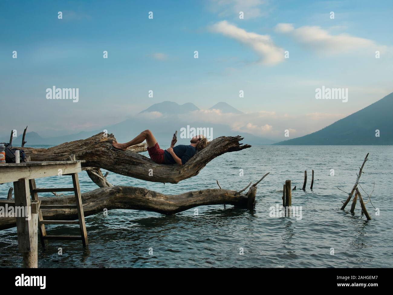 Handsome, casual man lying on a tree, reading in nature. Outdoor lifestyle, solo travel, recreational, free time, educational concept. Lake Atitlán Stock Photo