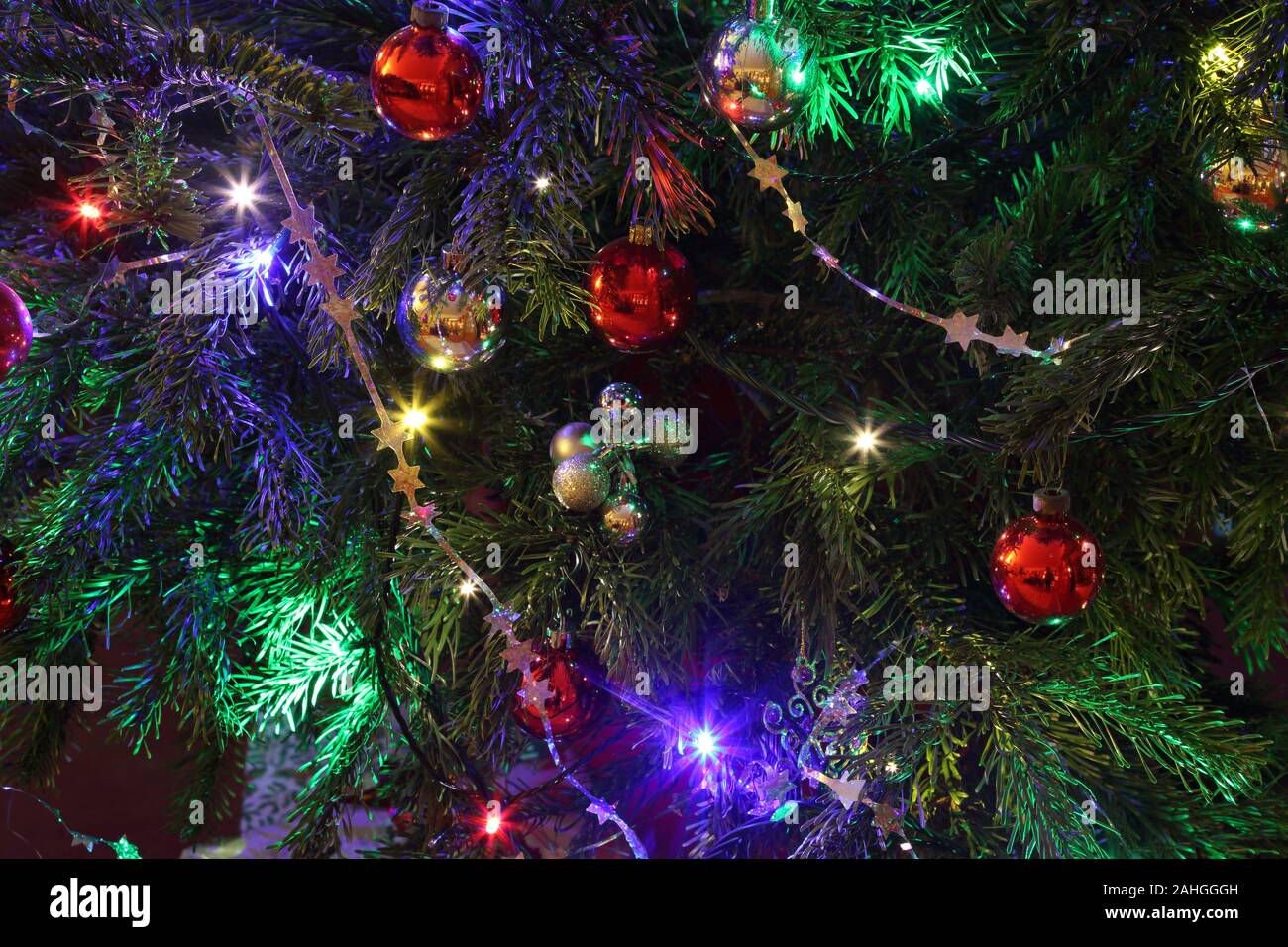 Close-up of part of a Christmas tree with decorations, Christmas baubles, tinsel, stars, and fairy lights, Haslemere, Surrey, UK. Stock Photo