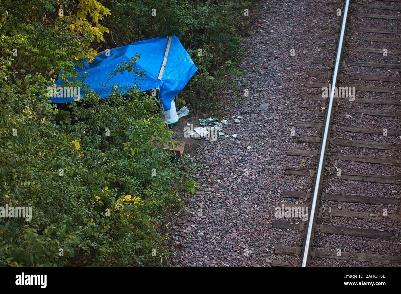 A temporary homeless shelter with a blue plastic tarp for a roof alongside a railroad track Stock Photo