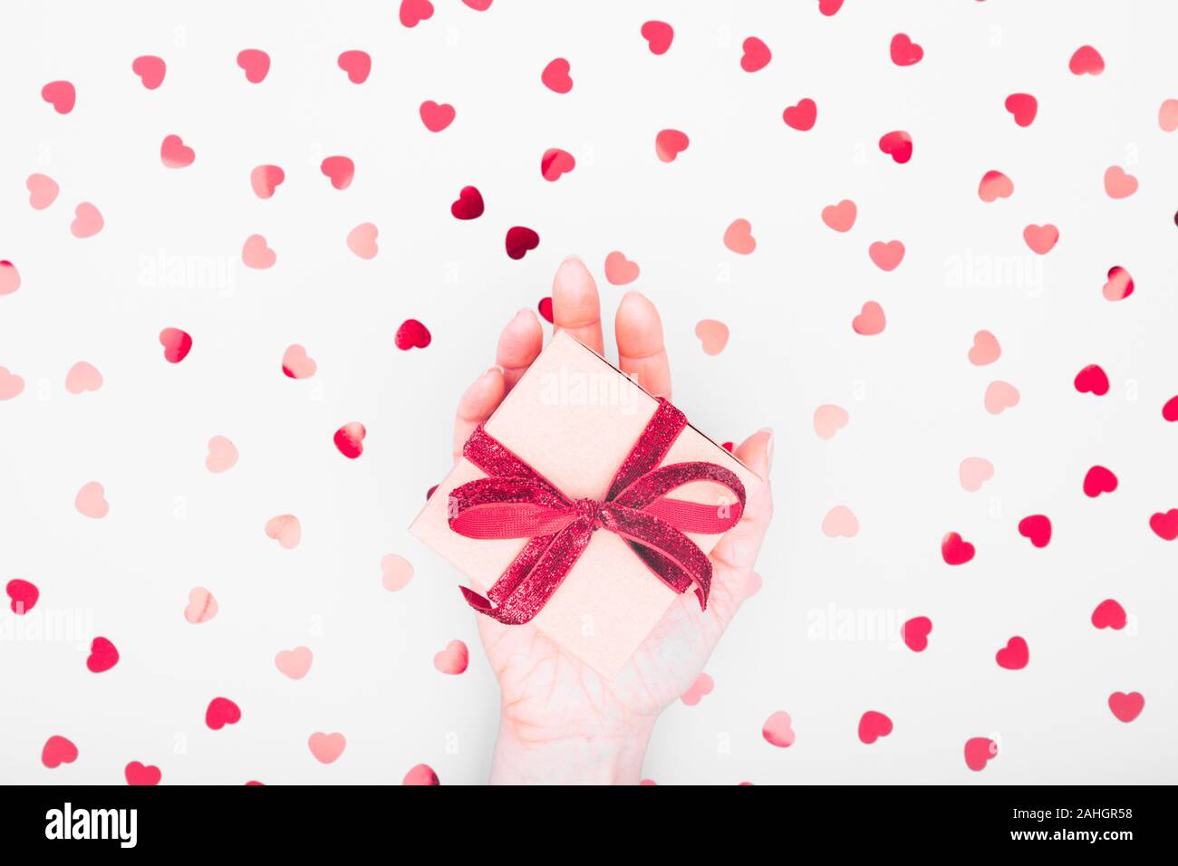 Craft box with red ribbon bow in female hand. Valentine day and eco ...