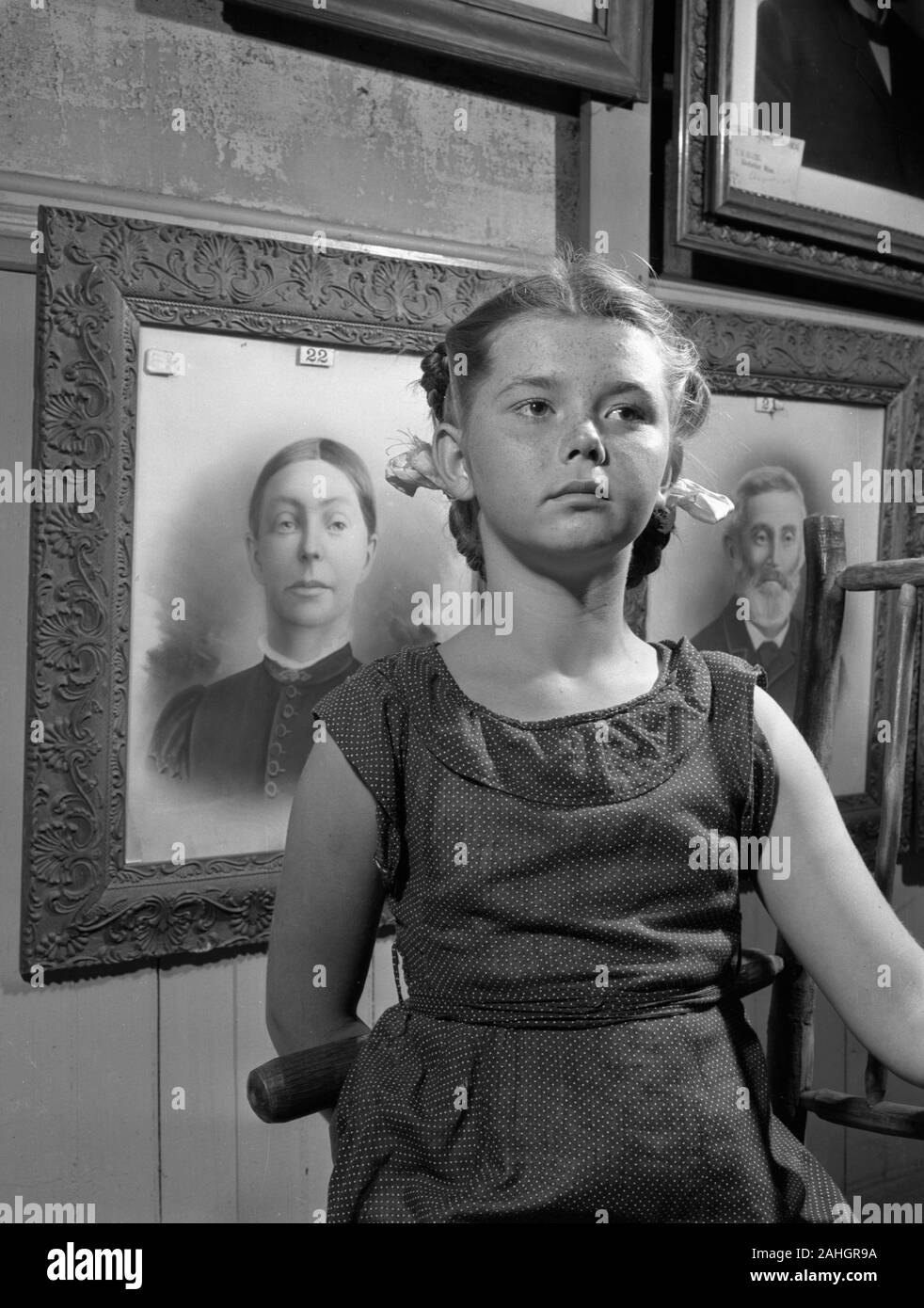 Girl standing in front of portraits of family members, 1946. This was part of the Minnesota State Fair in 1946, where people stood in front of portraits of their grandparents to illustrate genealogical traits. Stock Photo