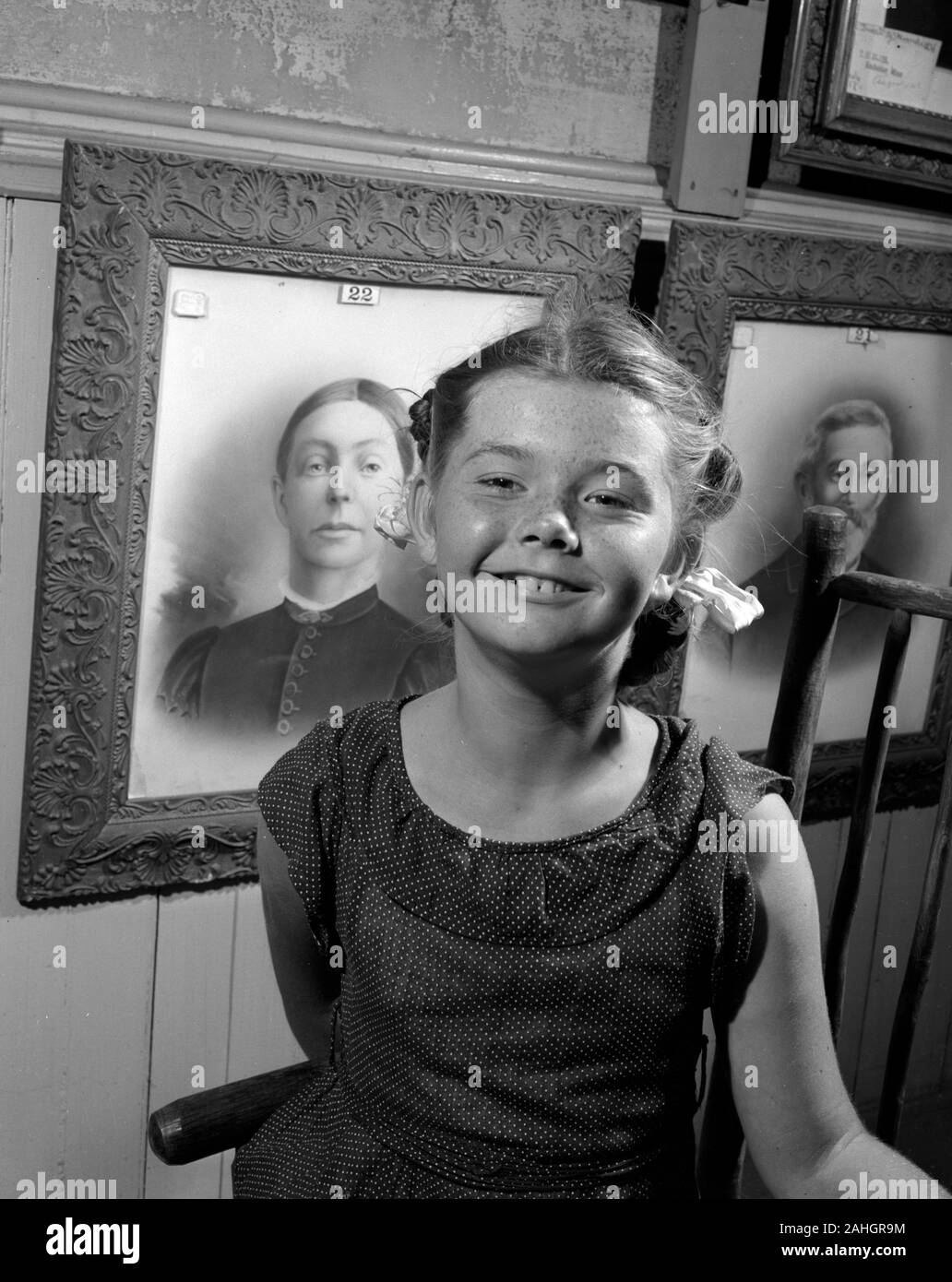 Girl standing in front of portraits of family members, 1946. This was part of the Minnesota State Fair in 1946, where people stood in front of portraits of their grandparents to illustrate genealogical traits. Stock Photo