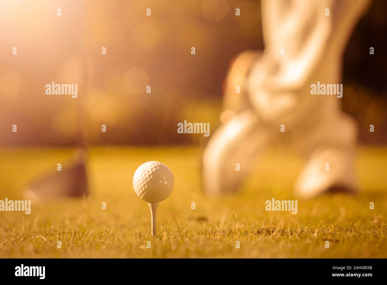 close up on golf ball on tee with golfers shoes and one wood low angle sun flare background Stock Photo