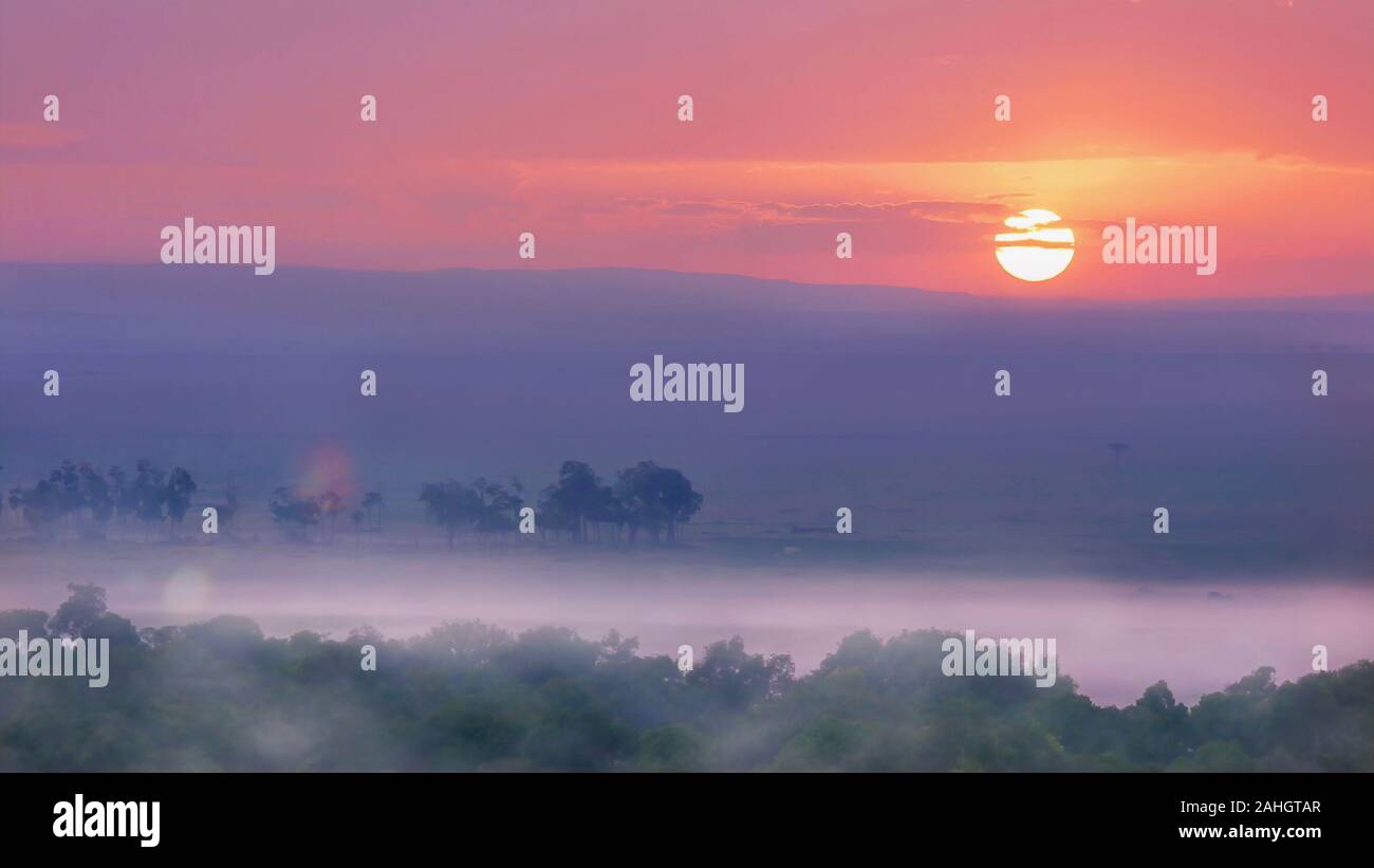 An African sunrise over the Masai Mara in Kenya, with  a soft focus misty landscape on the ground, shot from a hot air balloon. Stock Photo