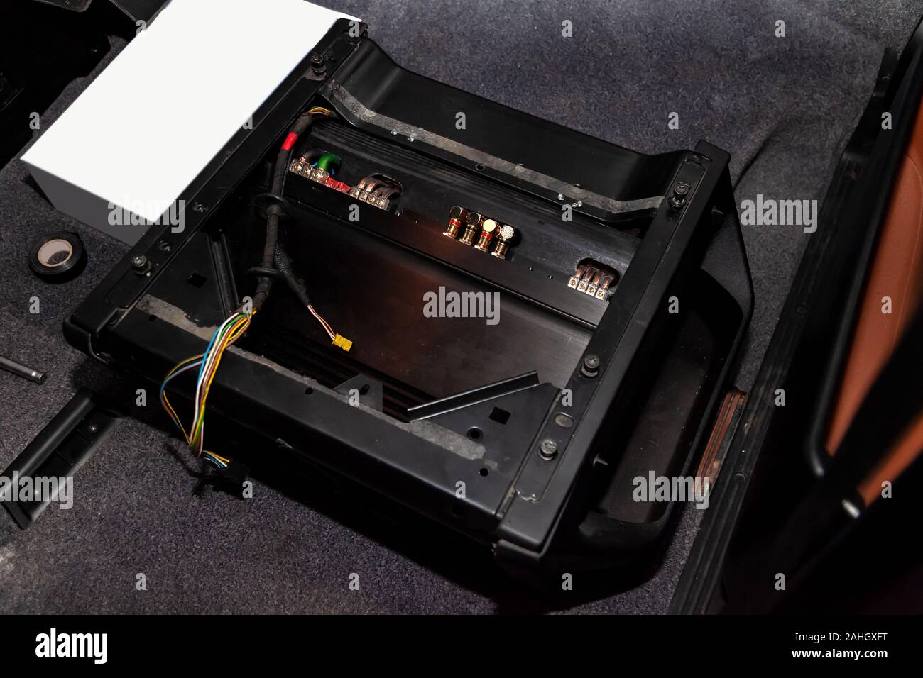 The amplifier of the car audio system in a black metal housing mounted on the floor of the vehicle in a repair and tuning workshop. Auto service indus Stock Photo