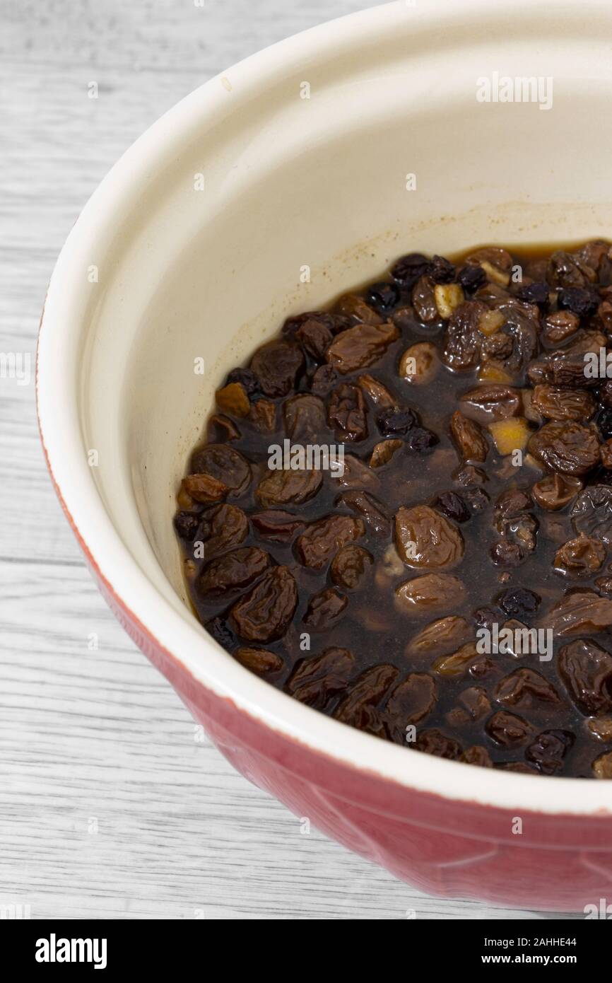 Mixed dried fruit soaking in a tea marinade in a mixing bowl. Grey wood