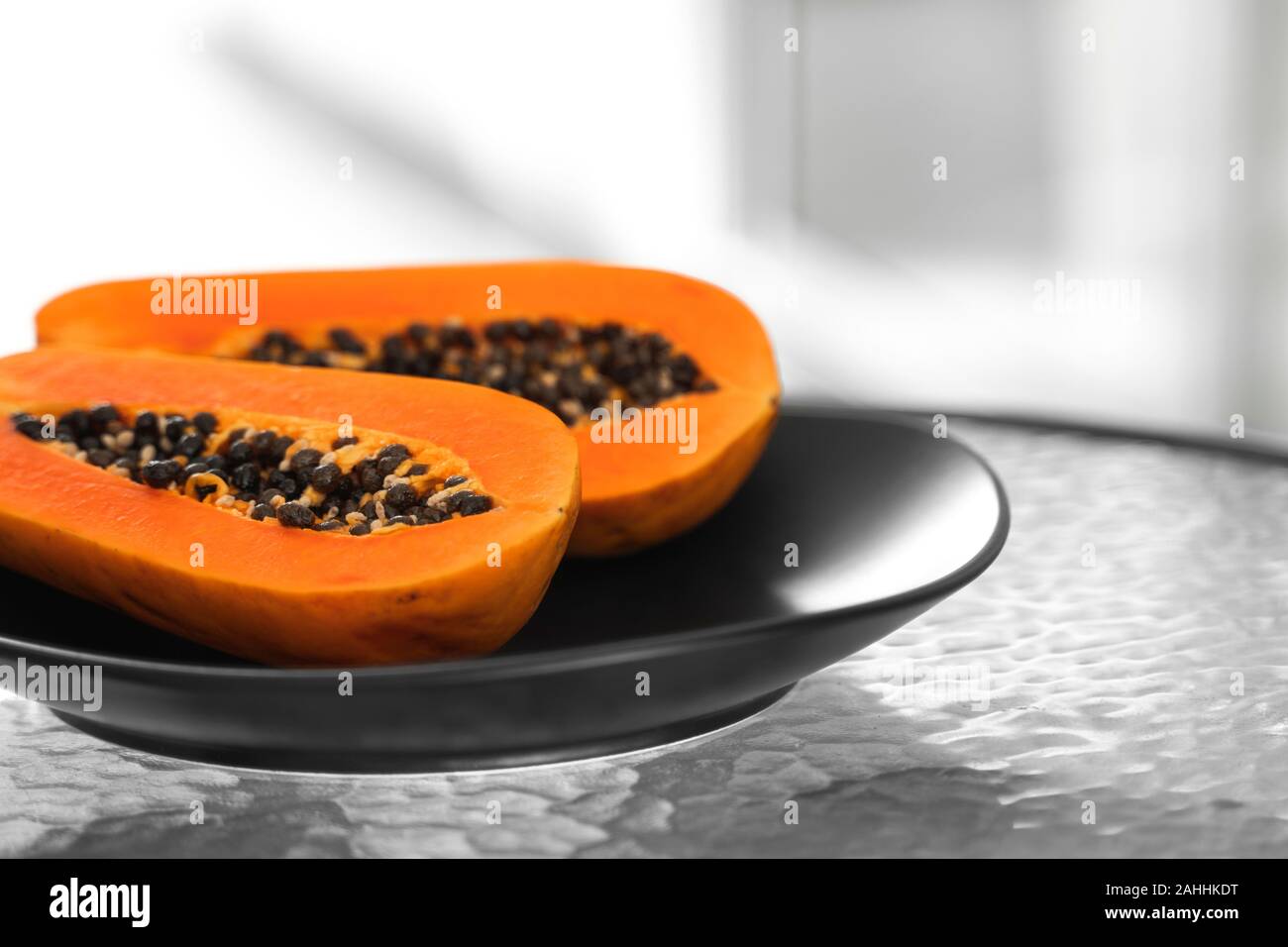 Two half of ripe papaya with seeds in a black plate on a glass table with a white background. Slices of sweet papaya image