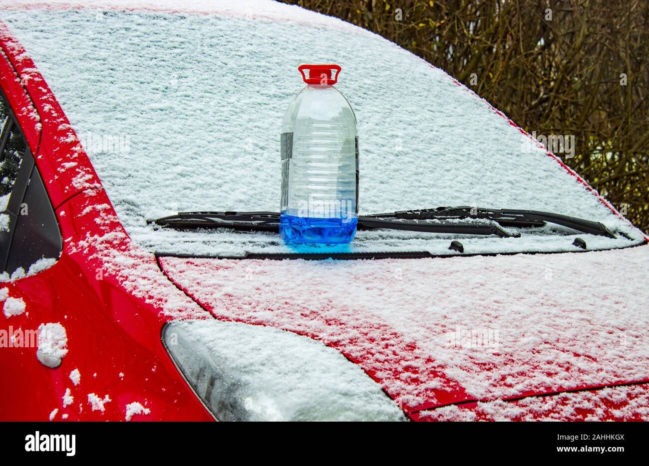 Windscreen washer antifreeze stands on front hood of red car in snow in winter. Stock Photo