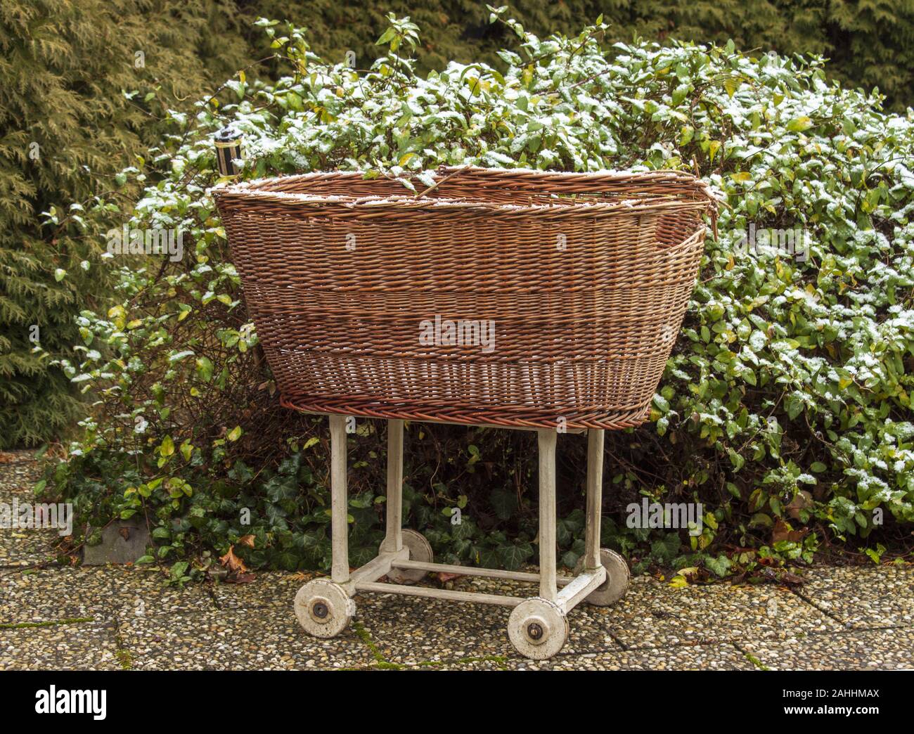 Old wicker basket for baby on wheels on the garden in winter. Stock Photo