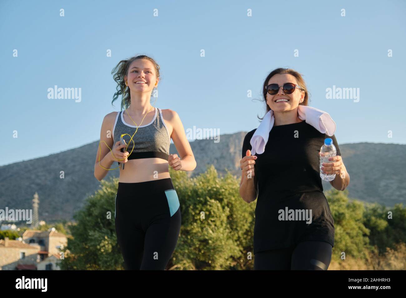 Two running women. Mother and daughter teenager running outdoor on road in mountains on summer sunny day. Family, healthy active sport lifestyle. Stock Photo