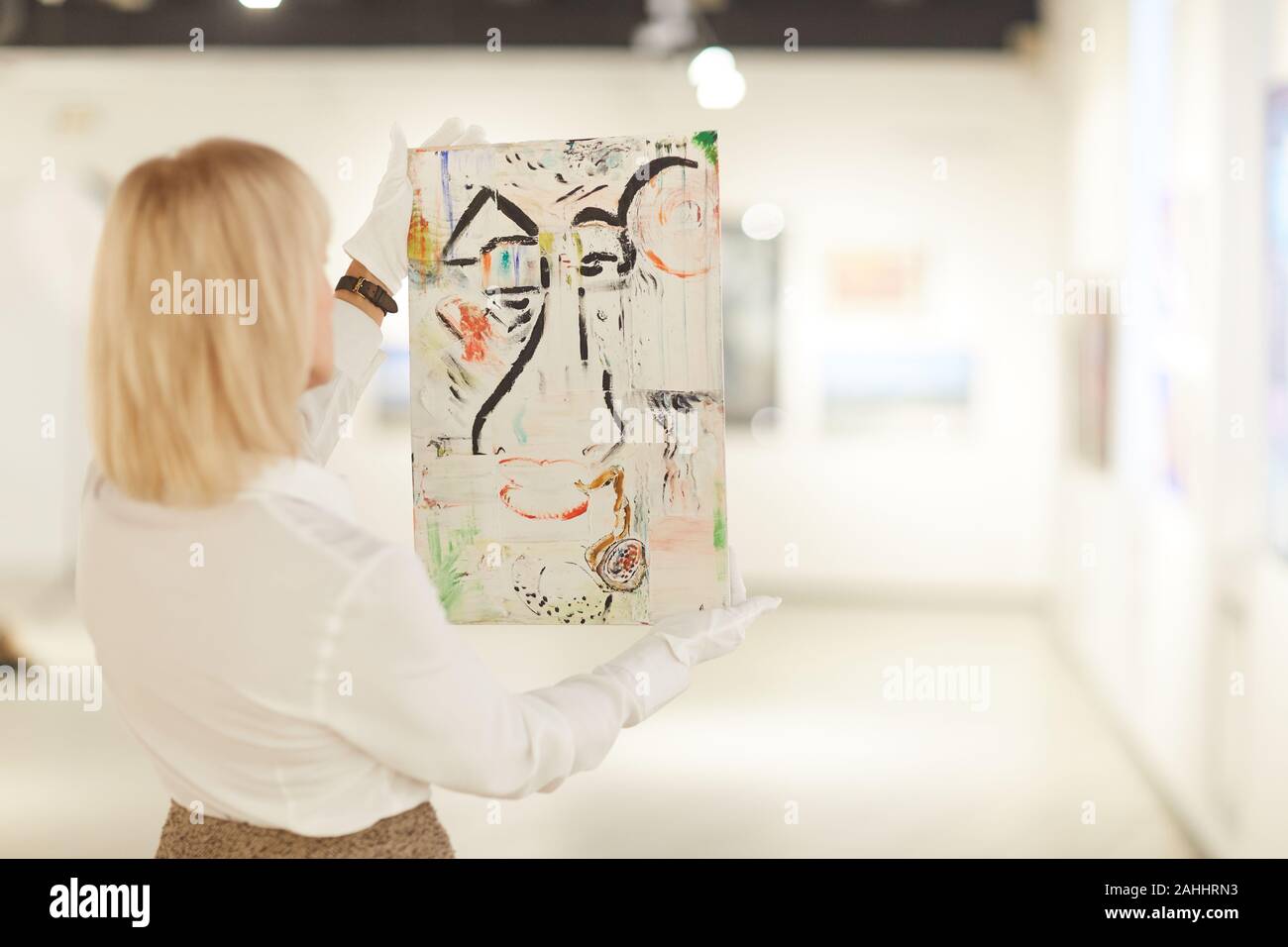 Back view portrait of female art expert holding painting while ...
