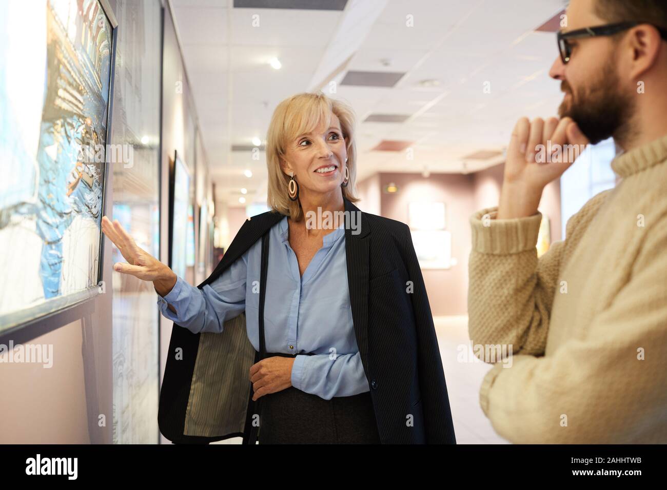 Waist up portrait of cheerful mature couple standing by paintings while enjoying exhibition in art gallery or museum Stock Photo